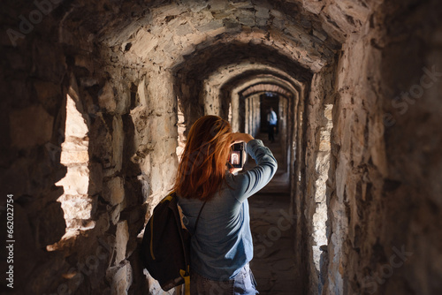 Woman walking through old tunnel, looking in window and taking pictures. Female visiting castle. Traveling in ancient building  © ninelutsk