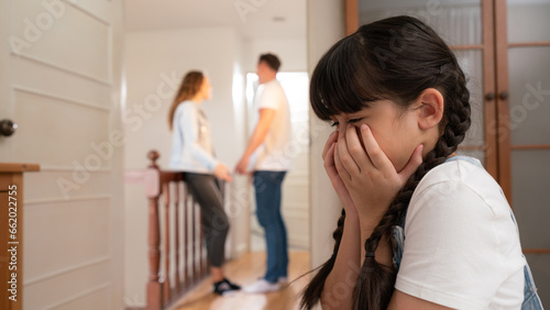 Stressed and unhappy young girl huddle in corner, cover her face while her parent arguing in background. Domestic violence at home and traumatic childhood develop to depression. Panorama Synchronos