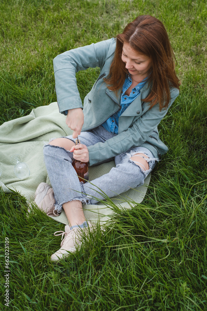 Woman uncork the bottle of rose wine on the picnic. Beautiful mature woman serve wine in glass outdoors on the grass. Woman at her 50s in the park Woman uncork the bottle of rose wine on the picnic. Beautiful mature woman serve wine in glass outdoors on the grass. Woman at her 50s in the park