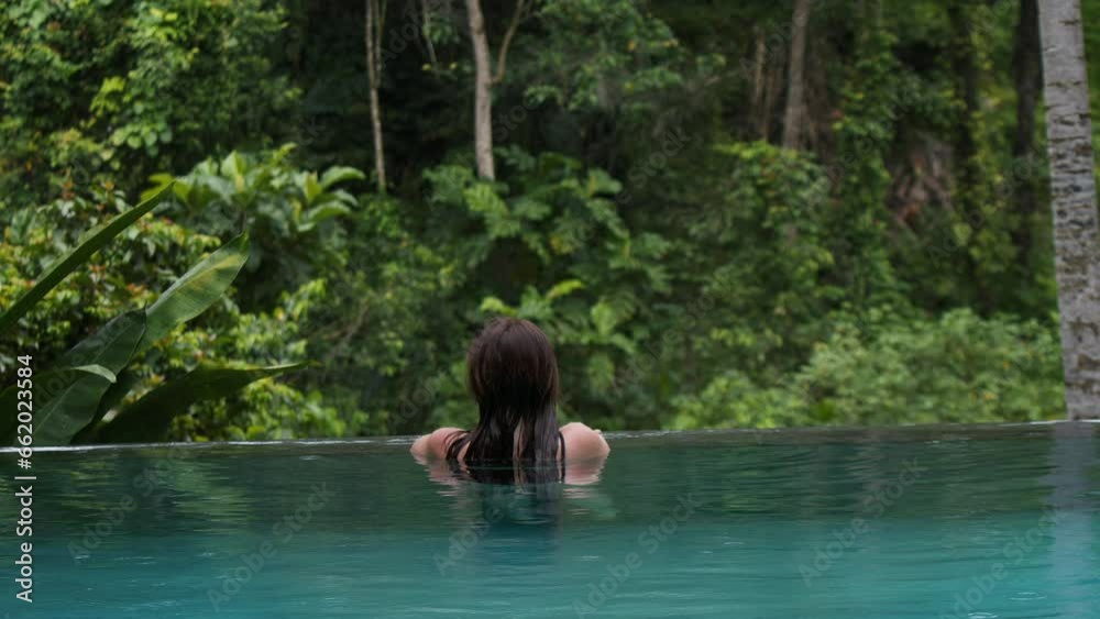 Attractive woman resting on the edge of infinity swimming pool, Rain in tropical forest, jungle, concept of tranquility, copy space. Attractive woman resting on the edge of infinity swimming pool, Rain in tropical forest, jungle, concept of tranquility, copy space.