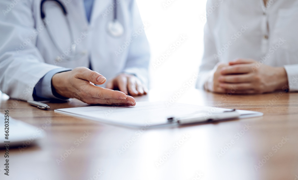 Doctor and patient discussing something while sitting near each other at the wooden desk in clinic. Medicine concept Doctor and patient discussing something while sitting near each other at the wooden desk in clinic. Medicine concept