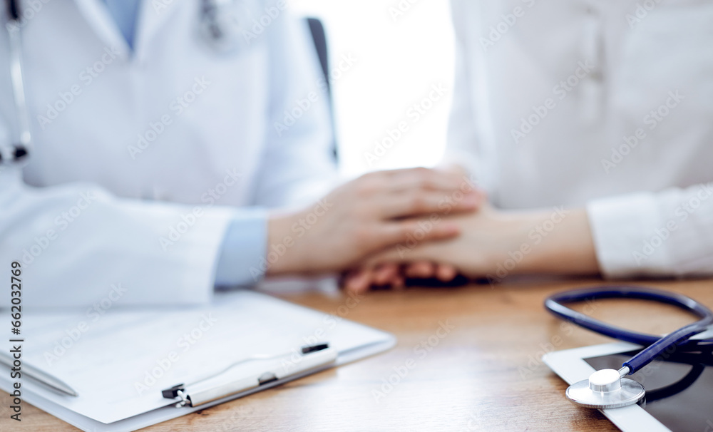 Stethoscope and tablet computer are lying on the wooden table while doctor's hands reassuring a patient at the background. Medicine concept Stethoscope and tablet computer are lying on the wooden table while doctor's hands reassuring a patient at the background. Medicine concept