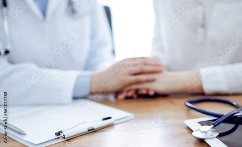 Stethoscope and tablet computer are lying on the wooden table while doctor's hands reassuring a patient at the background. Medicine concept