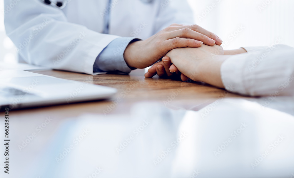 Doctor and patient sitting at the wooden table in clinic. Female physician's hands reassuring woman. Medicine concept Doctor and patient sitting at the wooden table in clinic. Female physician's hands reassuring woman. Medicine concept