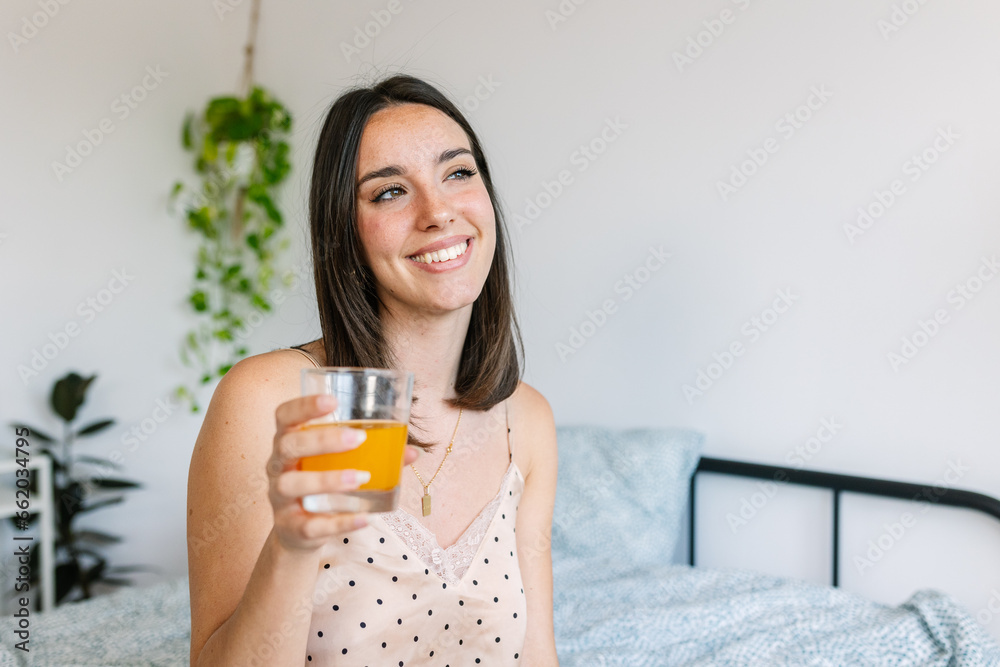 Young beautiful woman in pajama sitting on bed drinking orange juice. Healthy lifestyle concept. Young beautiful woman in pajama sitting on bed drinking orange juice. Healthy lifestyle concept.