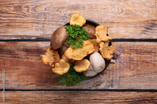 Bowl of different mushrooms and parsley on wooden table, top view