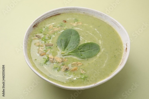 Delicious broccoli cream soup with basil and pumpkin seeds on green background, closeup