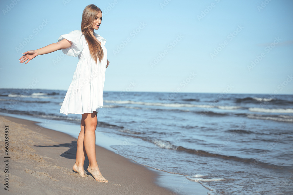 Happy smiling beautiful woman is walking on the ocean beach with open arms Happy smiling beautiful woman is walking on the ocean beach with open arms