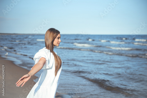 Happy  beautiful woman on the ocean beach standing in a white summer dress  open arms
