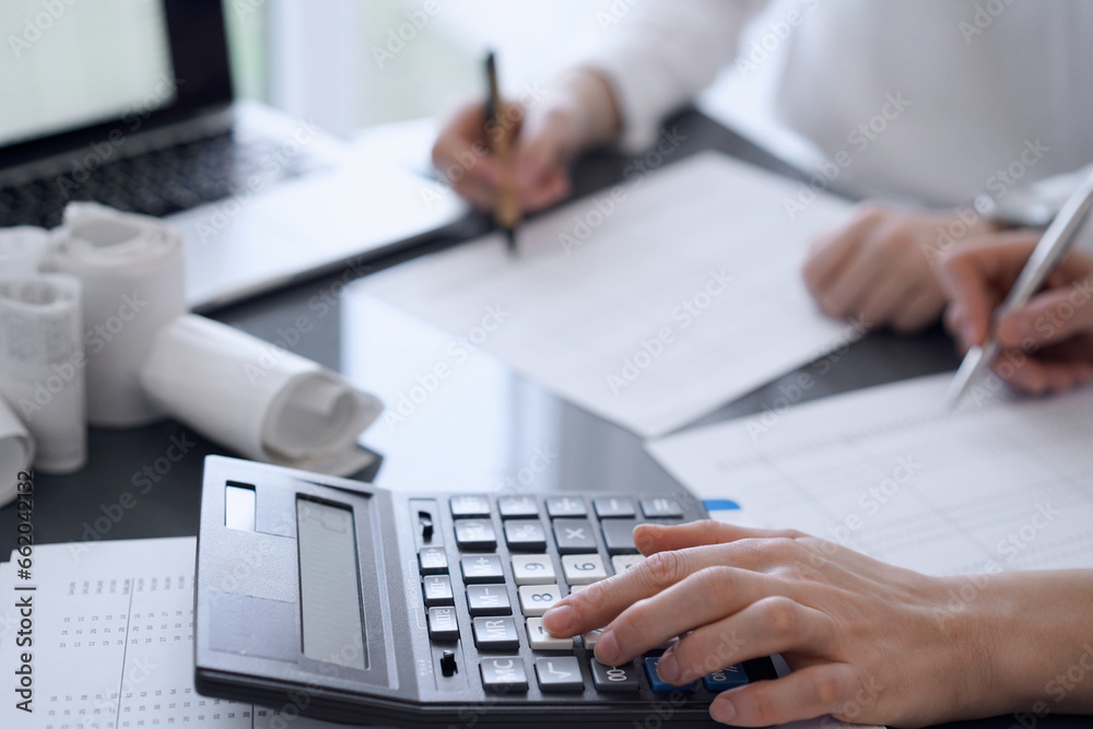 Fototapeta premium Two accountants use a calculator and laptop computer for counting taxes or revenue balance. Business, audit, and taxes concepts