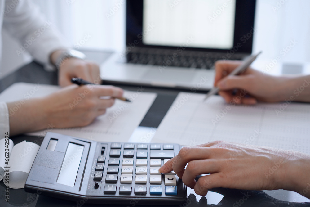 Fototapeta premium Two accountants use a calculator and laptop computer for counting taxes or revenue balance. Business, audit, and taxes concepts
