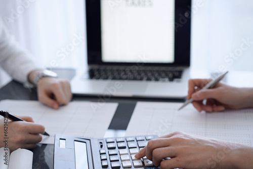 Two accountants use a calculator and laptop computer for counting taxes or revenue balance. Business, audit, and taxes concepts photo