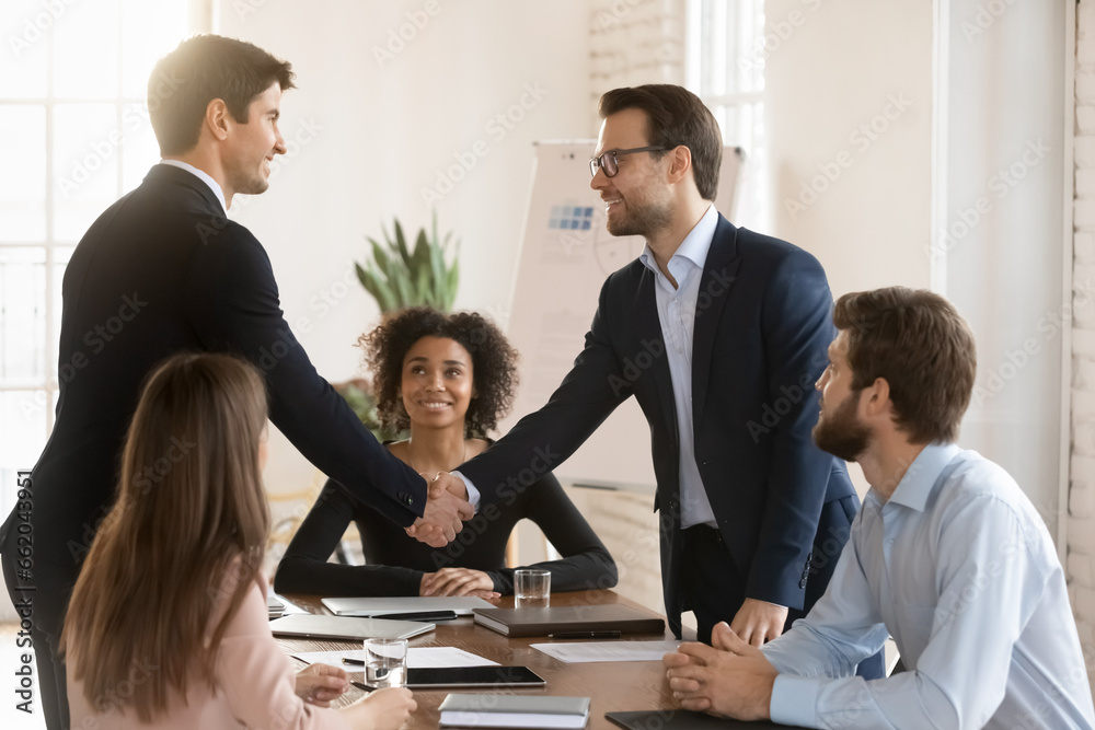 Two successful managers men in formal jackets greeting each other on team meeting, giving partnership handshake after discussing collaboration, teamwork, closing business deal, agreement Two successful managers men in formal jackets greeting each other on team meeting, giving partnership handshake after discussing collaboration, teamwork, closing business deal, agreement