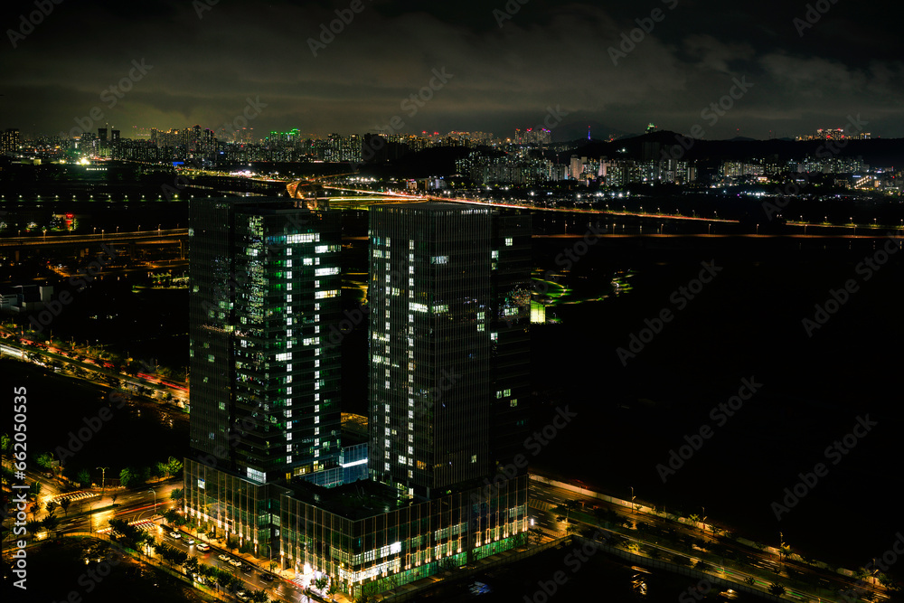 Incheon City Skyline at night in South Korea, tall clusters of illuminated buildings on the dark cloudy sky with the view of Seoul over the distant mountains Incheon City Skyline at night in South Korea, tall clusters of illuminated buildings on the dark cloudy sky with the view of Seoul over the distant mountains