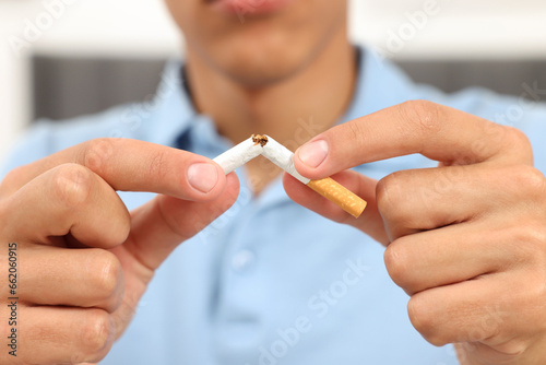 Stop smoking concept. Young man breaking cigarette on blurred background, closeup