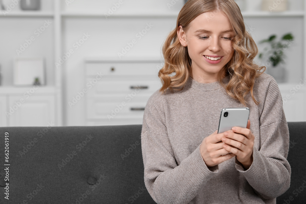 Beautiful woman with blonde hair using smartphone on sofa indoors. Space for text Beautiful woman with blonde hair using smartphone on sofa indoors. Space for text