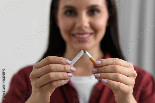 Stop smoking concept. Young woman breaking cigarette on blurred background, selective focus