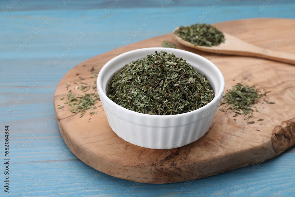 Bowl with dry tarragon and spoon on light blue wooden table Bowl with dry tarragon and spoon on light blue wooden table