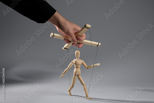 Man pulling strings of puppet on gray background, closeup photo