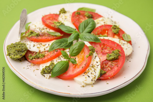 Plate of delicious Caprese salad and spoon with pesto sauce on green table, closeup