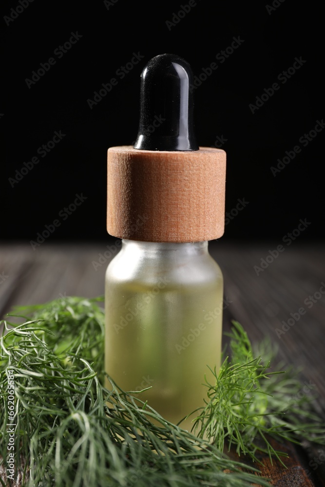 Bottle of essential oil and fresh dill on wooden table, closeup