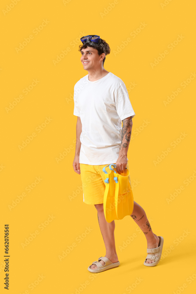 Fototapeta premium Young man with snorkeling mask and flippers on yellow background