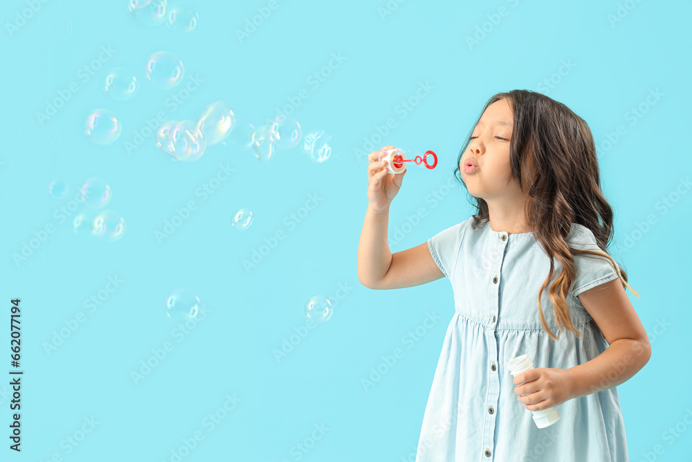 Cute little girl blowing soap bubbles on light blue background Cute little girl blowing soap bubbles on light blue background