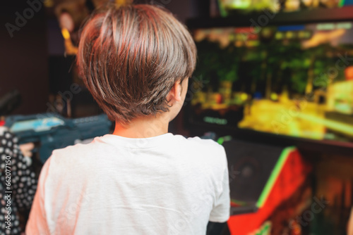 Kids play slot machine at amusement theme park, children play arcade gaming machine, racing and shooting game at the fair, teenagers having fun playing simulator video games