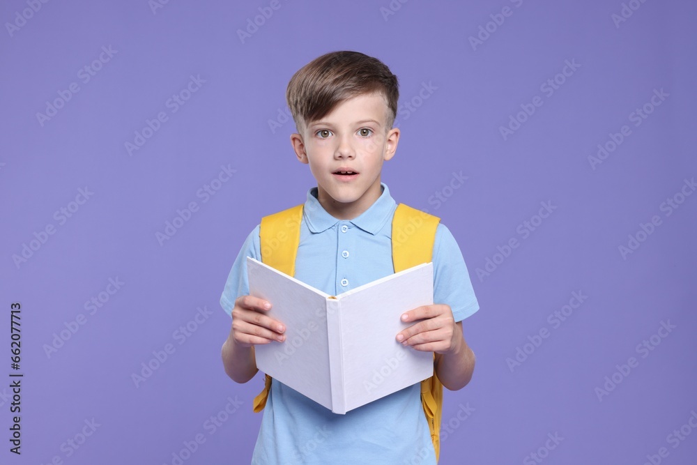 Cute schoolboy with book on violet background Cute schoolboy with book on violet background