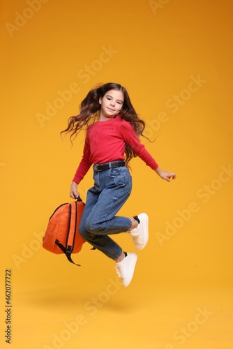 Back to school. Cute girl with backpack jumping on orange background