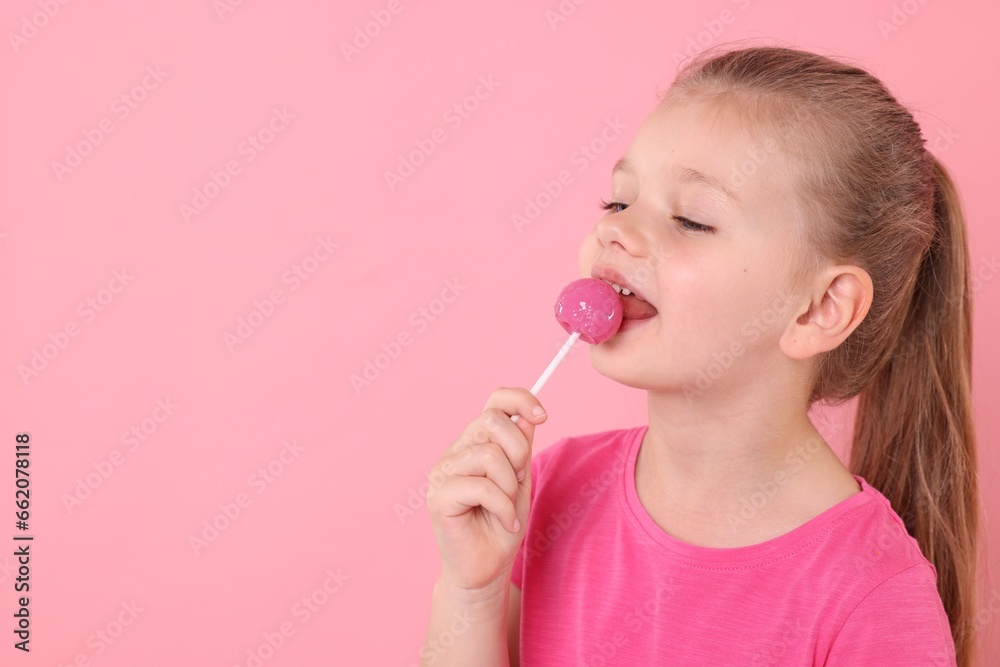 Cute little girl licking lollipop on pink background, space for text Cute little girl licking lollipop on pink background, space for text