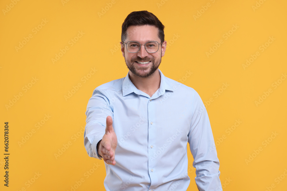 Happy man welcoming and offering handshake on yellow background - obrazy, fototapety, plakaty 