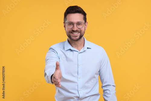 Happy man welcoming and offering handshake on yellow background