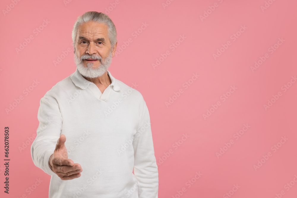 Senior man welcoming and offering handshake on pink background, space for text Senior man welcoming and offering handshake on pink background, space for text