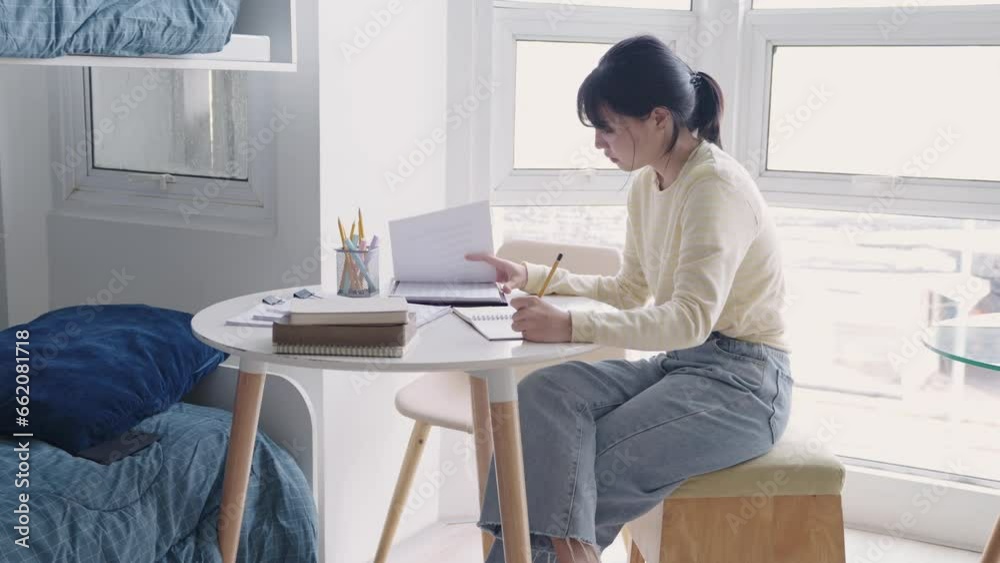 A college student does her homework writing preparing for exam test while studying paper textbook at her desk in dorm. A college student does her homework writing preparing for exam test while studying paper textbook at her desk in dorm.