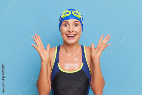 Εκτύπωση καμβά Cute happy swimmer in swimsuit and cap smiles joyfully with her hands up, profes