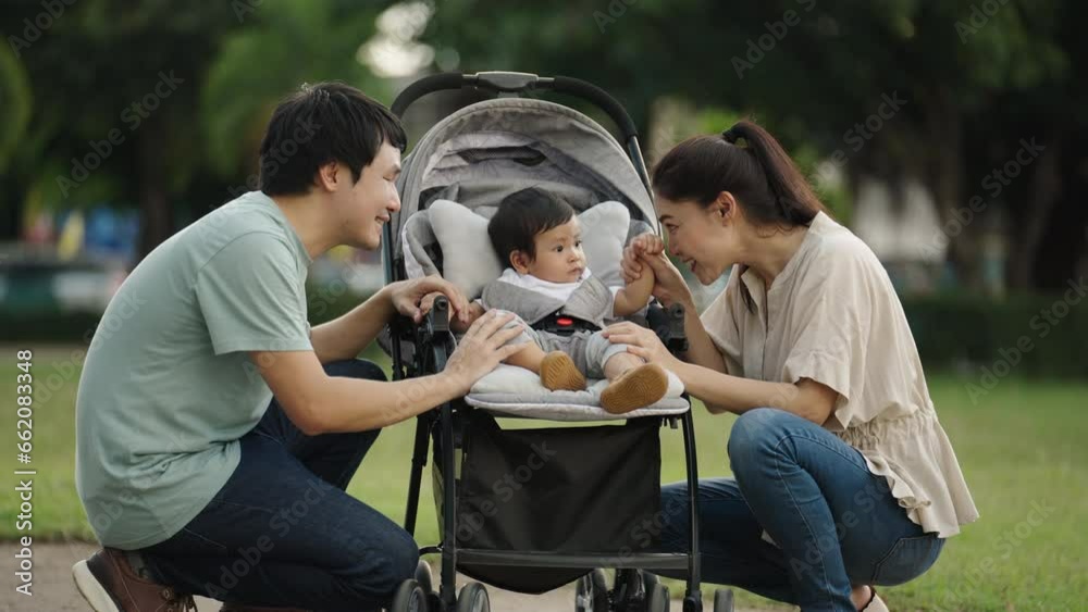 happy parent (father and mother) talking and playing with infant baby in the stroller while resting in park happy parent (father and mother) talking and playing with infant baby in the stroller while resting in park