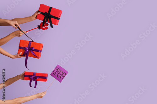 Women with Halloween gifts, wand and word BOO on lilac background