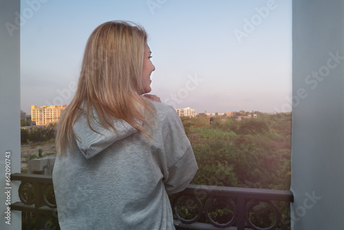 A girl stands on the balcony and looks at the sunset