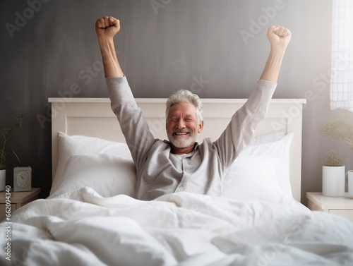 Happy old man in nightwear in bed feel good, stretching her arms muscles after sleep photo