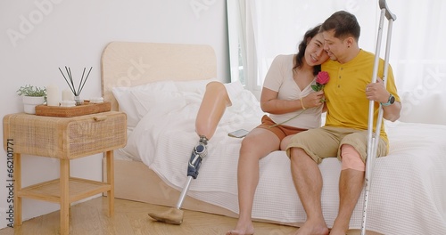 Happy Asian woman wearing prosthetics leg and couple man with leg disabilities spend time to celebrate anniversary and valentine day together, man surprise and give rose flower to beautiful girlfriend