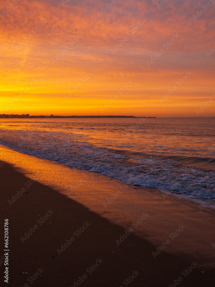 Amazing view of a fiery sunrise with multicolored clouds. Sea waves along the seashore at sunrise. Morning time. Ocean view. La Baule-Escoublac, France
