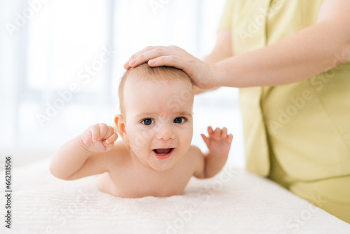Portrait of adorable infant baby boy lying on stomach tummy, smiling looking at camera. Closeup of toddler training to keep head up, starting to crawl. Happy kid enjoying leisure physical activities.