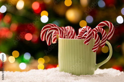 Mug with candy canes and christmas tree with fairy lights and copy space