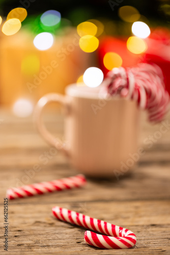 Vertical image of mug with candy canes and christmas tree with fairy lights and copy space