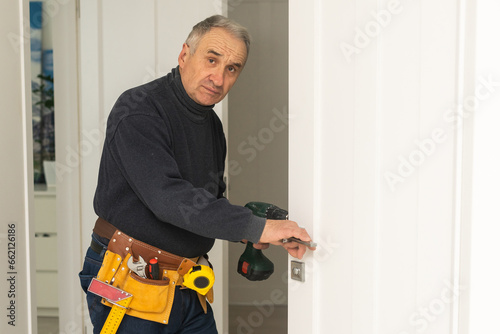 Ordinary elderly man independently repairs a door © Angelov