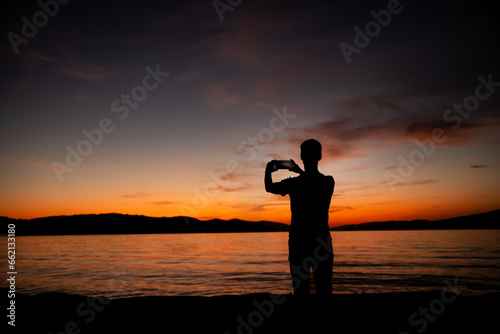 sylwetka mężczyzny robiącego zdjęcie zachodu słońca nad morzem