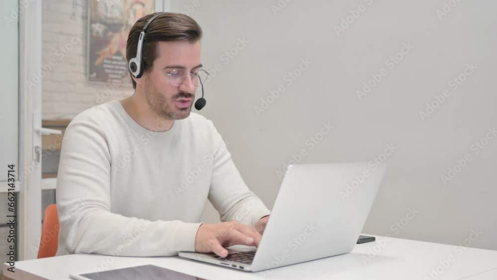 Young Man with Headset Doing Video Chat on Laptop in Call Center