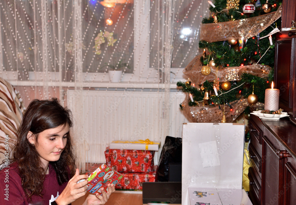 A young girl unwraps Christmas presents from under the Christmas tree at home