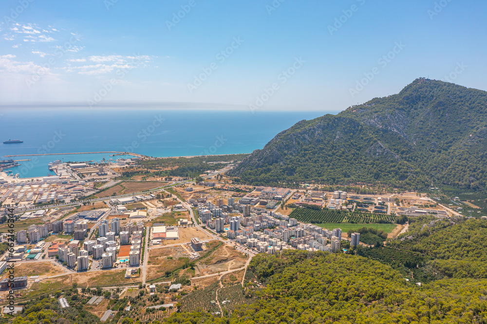 Fototapeta premium Flight over ridge mountain pass rocky terrain with bushes, bird's eye view overlooking the city, houses and buildings, roads and ships, Mediterranean coast, resort area, vacation trip.